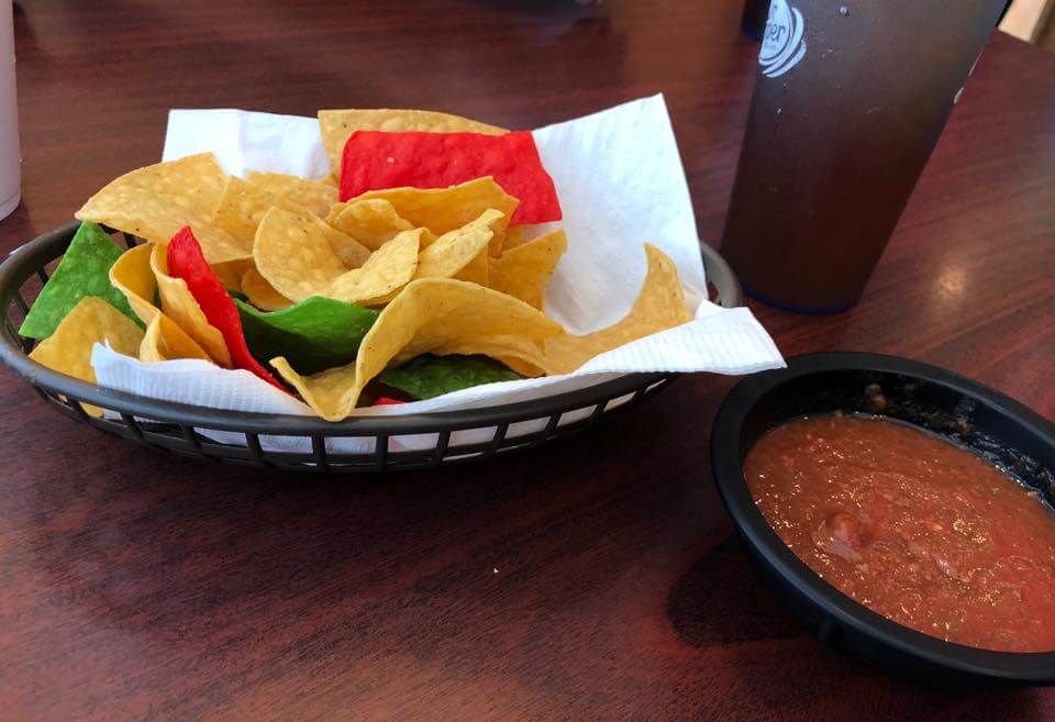 A basket of yellow, red and green tortilla chips with a bowl of house salsa