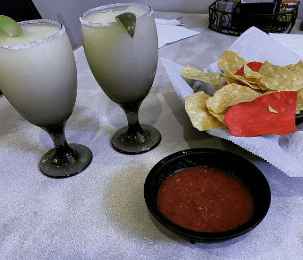 Two frozen lime margaritas with salted rims next to tortilla chips and salsa